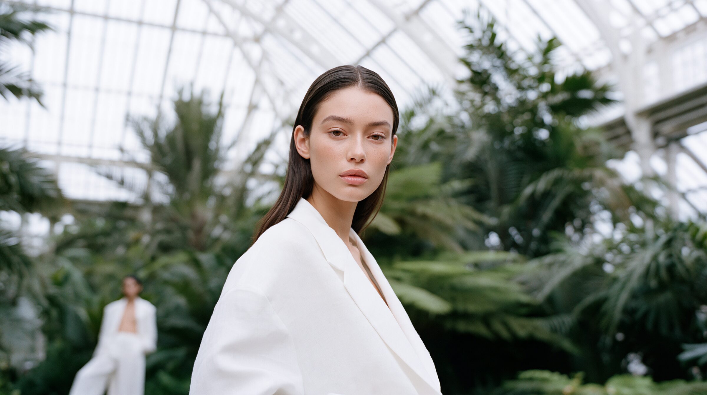 Model in an ivory linen suit standing small among towering palms beneath a curved glass roof