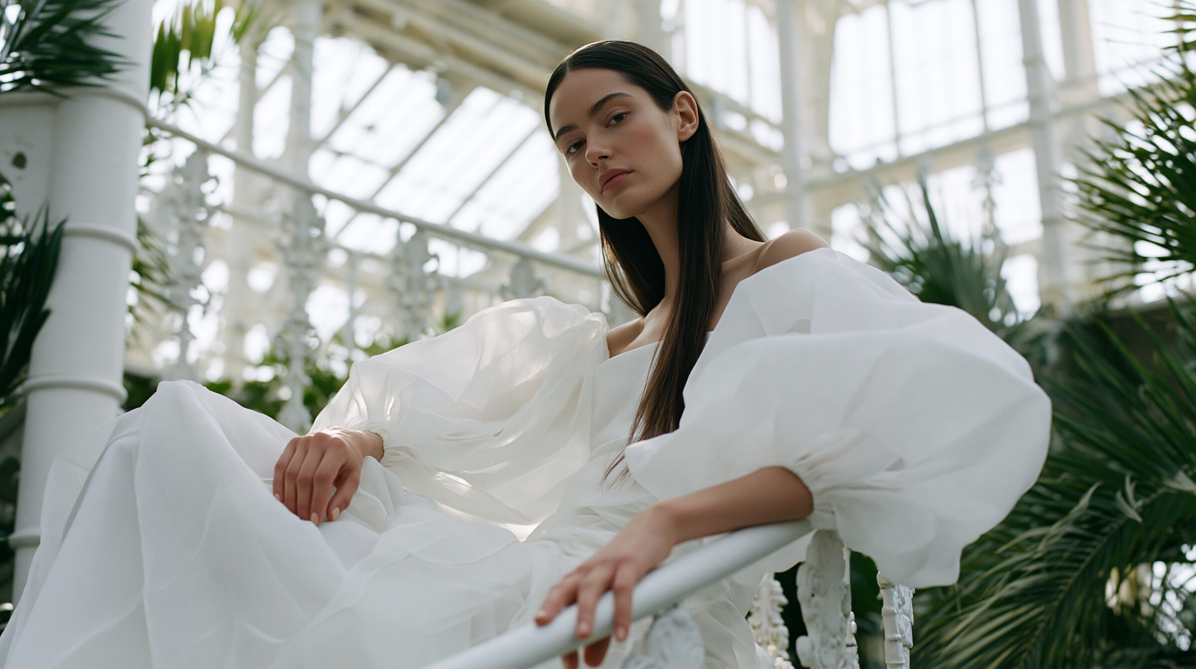 Model in an ivory organza gown seated on a white spiral iron staircase at golden hour