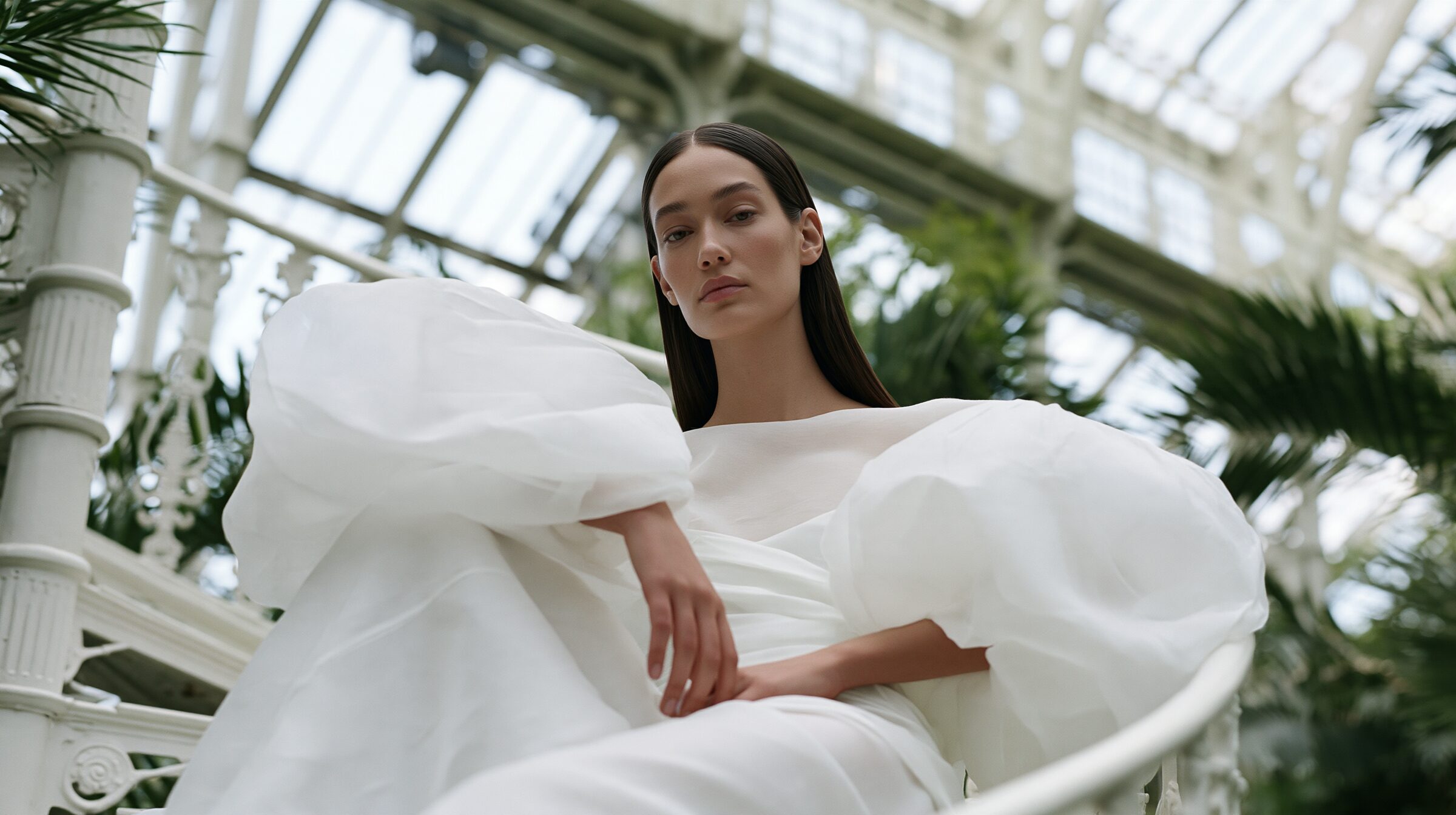 Model in an ivory organza gown seated on a white spiral iron staircase at golden hour