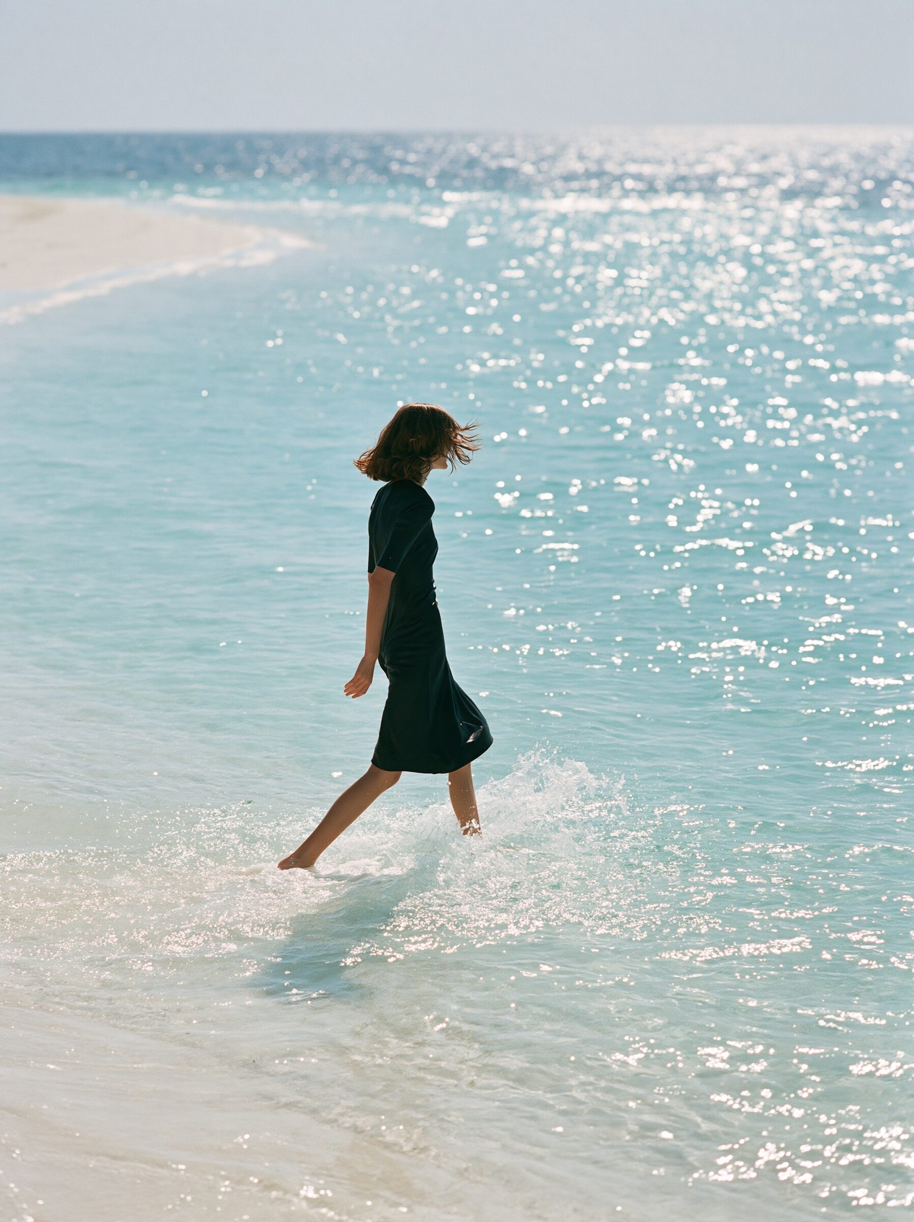 Model laughing as she wades knee-deep through crystal-clear turquoise water