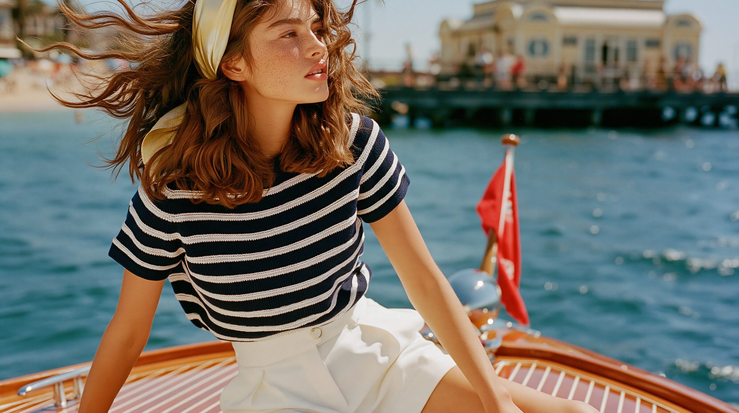 Model seated at the bow of a vintage mahogany speedboat, the Sorrento cliffs behind her